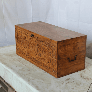 A rectangular storage chest crafted from solid wood, featuring a natural, warm brown finish with prominent wood grain and knot details. The chest has a hinged lid that sits flush when closed, and dark, possibly forged iron, pull handles are visible on the short sides. The overall design suggests a rustic or farmhouse aesthetic, emphasizing natural materials and robust construction. — 3D model