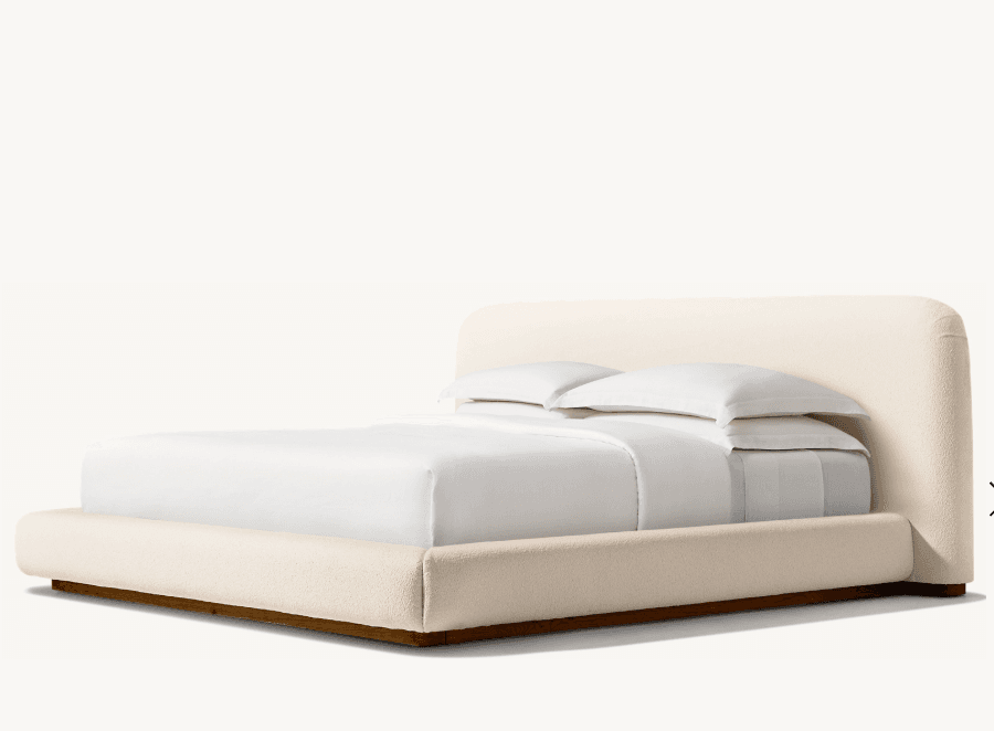 A low-profile bed frame with a rounded headboard and platform base, upholstered in a textured, light-colored fabric. The bed is dressed with white bedding, including two pillows stacked neatly. — 3D model