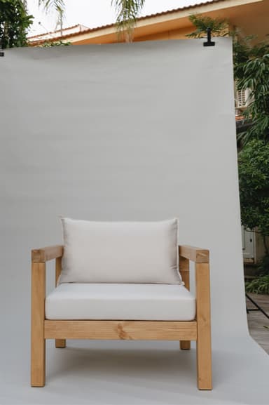 A single armchair with a solid wood frame and upholstered cushions. The frame consists of thick, square-profile wooden beams for the legs, base, and arms. The seat and back are padded with white cushions. A rectangular lumbar pillow is placed against the back cushion. — 3D model