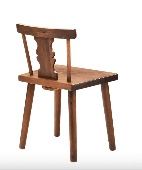 A rustic wooden chair with four tapered legs, a flat seat, and a backrest. The backrest features a decorative carved element with three scalloped curves in the center, supported by two vertical posts. The overall construction suggests a handmade or artisanal origin. — 3D model