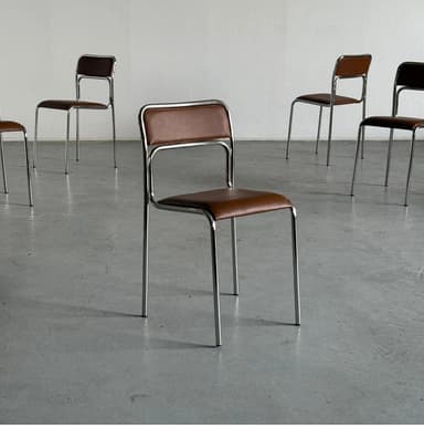 A modern chair with a tubular chrome-plated metal frame and brown upholstered seat and backrest. The frame consists of four legs, a seat support structure, and a backrest frame that connects to the rear legs. The seat and backrest appear to be padded and covered in a faux leather or vinyl material. — 3D model