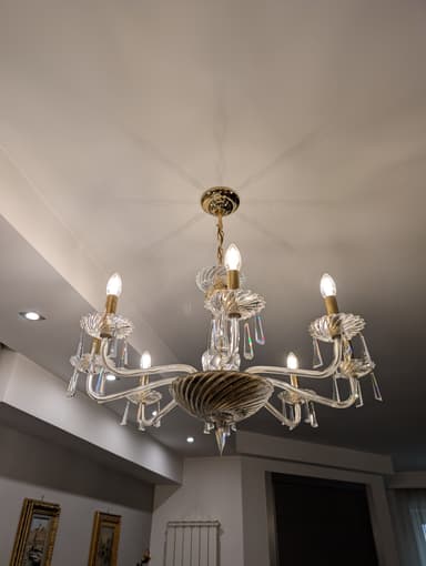 A multi-tiered chandelier with eight arms, featuring clear glass elements and crystal pendants. The central body has a twisted glass design, and the arms are curved, supporting candle-style light bulbs. The hardware appears to be gold-toned. — 3D model