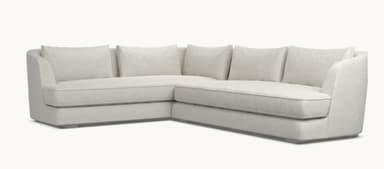 A modern sectional sofa with a light beige fabric upholstery. The sofa features a chaise lounge on the left and a sofa section on the right, with loose back cushions. The design is minimalist with clean lines and a low profile, supported by subtle metallic legs. — 3D model