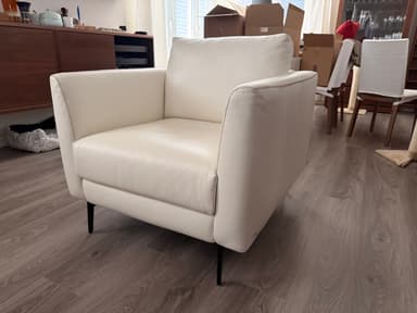 A modern white sofa with a tufted backrest and armrests, upholstered in a material that appears to be faux leather or high-quality vinyl. It features a clean, minimalist design with slim, black metal legs. The stitching detail is visible along the edges. — 3D model