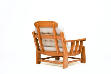 A sturdy, craftsman-style lounge chair featuring a solid oak wood frame and thick, upholstered cushions. The chair has broad, rounded arms, slatted side panels, and block legs. The back cushion is button-tufted. — 3D model