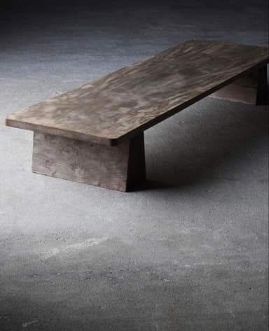 A low, rectangular bench constructed from dark, possibly stained wood, featuring a thick, solid top supported by two robust block-like legs. — 3D model