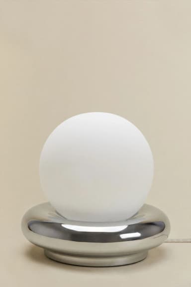 A modern table lamp featuring a spherical frosted white glass diffuser resting within a polished chrome base with a rounded, toroidal shape. The minimalist design emphasizes geometric forms and a sleek, reflective finish on the base, providing ambient light through the globe. — 3D model