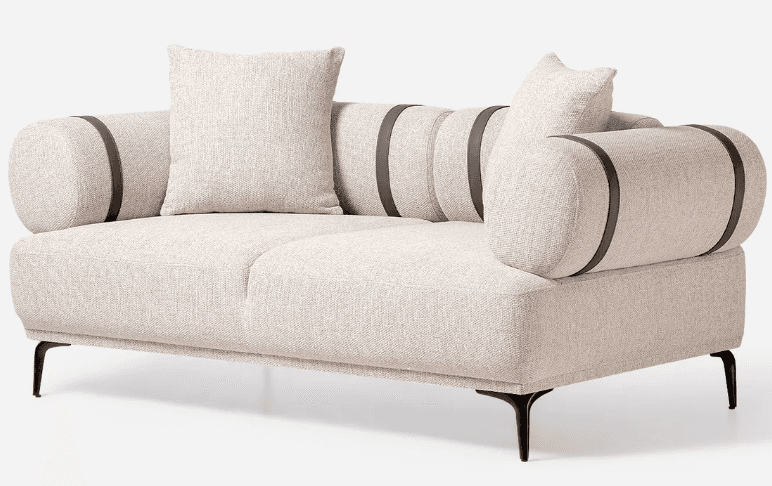 A modern two-seater loveseat featuring light beige textured fabric upholstery. It has distinctive cylindrical bolster arms, which are accented with dark, presumably leather or faux leather, straps. The loveseat includes two square loose throw pillows in the same fabric. It is supported by slender, splayed black metal legs, giving it an elevated and airy appearance. The overall design is clean, minimalist, and contemporary. — 3D model