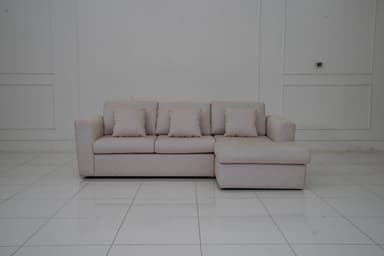 A sectional sofa with a chaise lounge extension, upholstered in a light-colored fabric with a subtle pattern. The sofa features three seat cushions and a chaise on the right side. It includes four matching throw pillows. The sofa has a modern, minimalist design with clean lines and low-profile arms and back. — 3D model