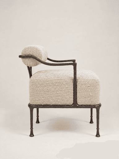 An accent chair featuring a dark, hammered or forged metal frame and upholstered in a light-colored, textured boucle-like fabric. The design includes a separate cylindrical bolster for the backrest and a rectangular cushion for the seat. The metal frame forms minimal armrests and sturdy, tapered legs with small feet. The overall aesthetic is modern and artisanal. — 3D model