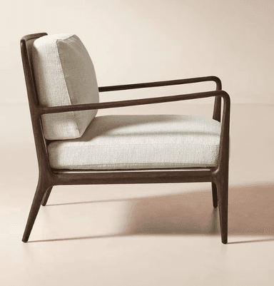 A contemporary armchair featuring a dark wood frame with a warm finish. The frame has a streamlined design with gently curved armrests that extend from the back. The chair is upholstered in a textured, off-white fabric on the seat, back cushion, and armrest pads. The overall design is minimalist and elegant, suitable for modern interiors. — 3D model