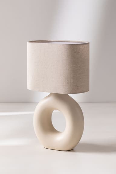 A modern table lamp featuring a cream-colored ceramic torus-shaped base with a central cut-out, topped with a cylindrical light beige fabric shade. — 3D model