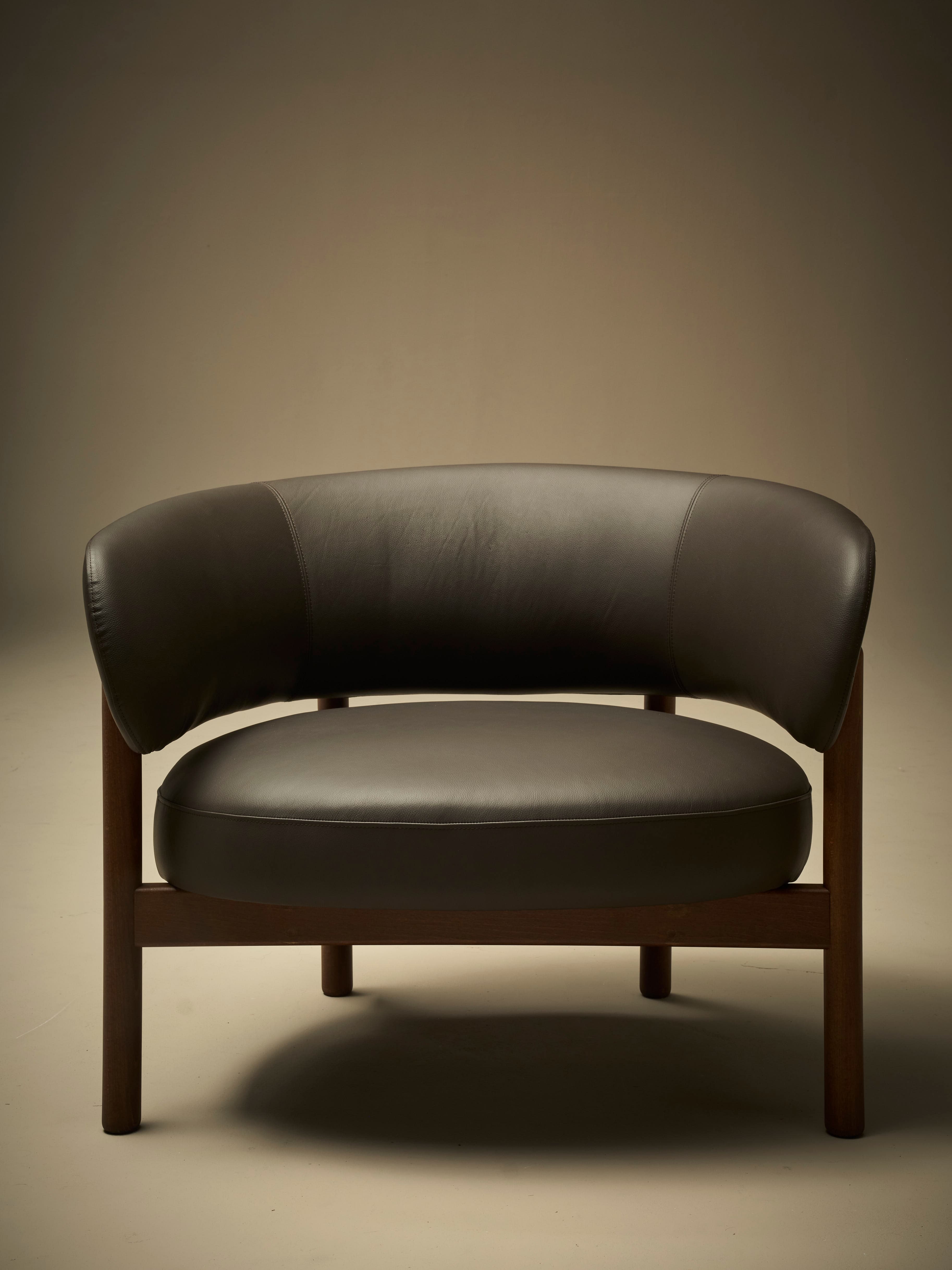 A low-profile armchair with a dark brown leather upholstered seat and curved backrest. The frame and legs are constructed from dark wood, exhibiting a minimalist design. The seat and back appear to be separate components supported by the wooden frame. — 3D model
