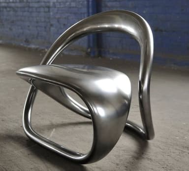 A modern, sculptural chair with a fluid, continuous form. It appears to be made from a single piece of material, shaped into a seat and a supporting backrest that curves upwards and forwards. The base is formed by loops that provide stability. — 3D model