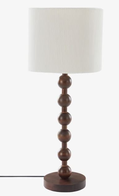 A table lamp featuring a distinctive dark wood base constructed from five stacked spherical elements, decreasing in size from bottom to top, atop a round, flat wooden pedestal. It is topped with a cylindrical drum shade made of white, vertically fluted material, providing diffused light. The design leans towards a modern or contemporary aesthetic with natural material accents. — 3D model