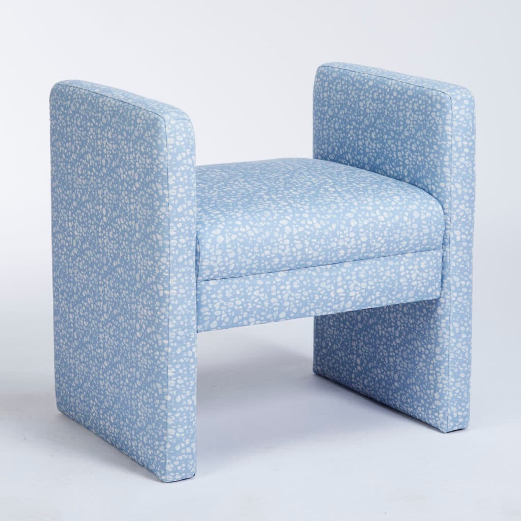 A compact, fully upholstered seating piece featuring a light blue fabric with a white speckled or terrazzo-like pattern. It has a rectangular seat supported by two solid, block-like structures that function as both legs and armrests, giving it a minimalist, integrated design. — 3D model
