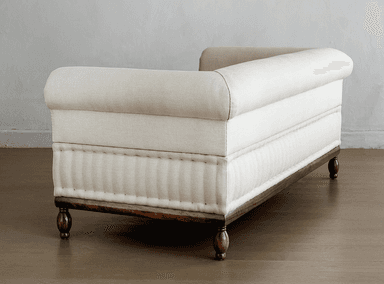 A cream-colored upholstered daybed with a rolled armrest and a tufted lower section. The daybed is supported by a dark wooden frame and features turned wooden legs. — 3D model
