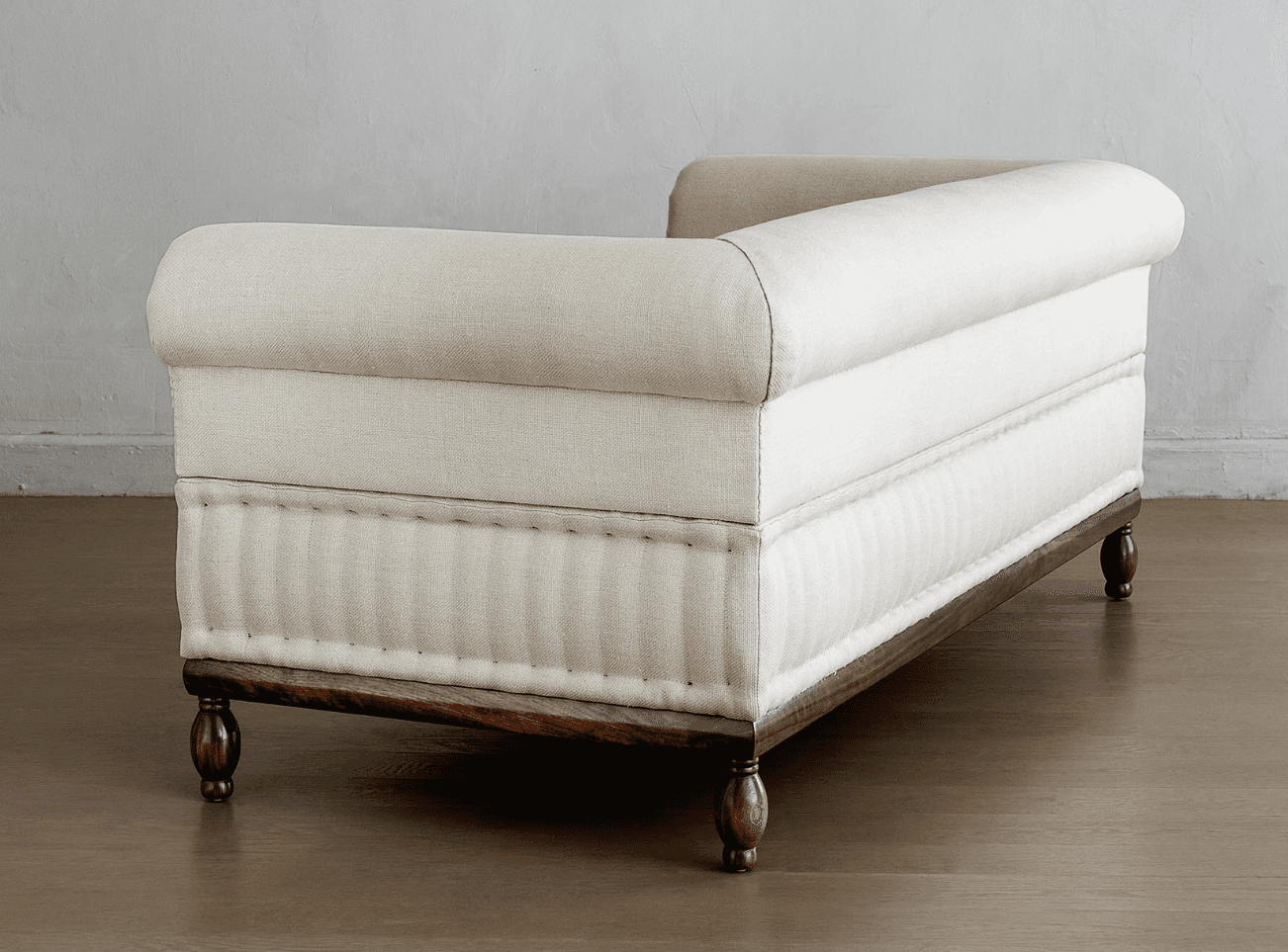 A cream-colored upholstered daybed with a rolled armrest and a tufted lower section. The daybed is supported by a dark wooden frame and features turned wooden legs. — 3D model