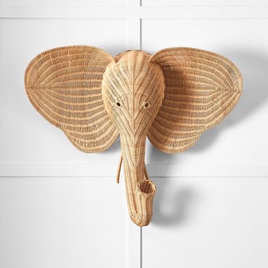 A natural-toned decorative wall sculpture in the shape of an elephant's head, intricately woven from wicker or rattan. The piece features large, flared ears and a distinctive, curled trunk, all crafted with visible woven texture, suggesting it is designed for wall mounting as a decorative accent. — 3D model