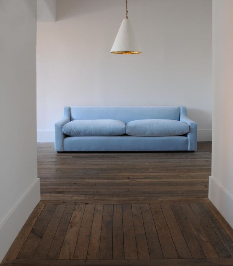 A contemporary two-seater sofa upholstered in a light blue fabric. It features a streamlined design with recessed, slightly flared arms that curve into the backrest. The sofa has two plush seat cushions and appears to have a low-profile base or concealed feet, emphasizing its clean lines. — 3D model