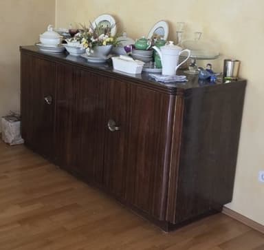 A rectangular, low-profile wooden sideboard or credenza featuring three cabinet doors. It is finished in a dark brown wood veneer with a distinct grain pattern and is fitted with small, circular, silver-toned knob handles. The design incorporates subtle rounded edges on the top and sides, resting on a recessed plinth base. — 3D model