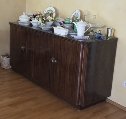 A rectangular, low-profile wooden sideboard or credenza featuring three cabinet doors. It is finished in a dark brown wood veneer with a distinct grain pattern and is fitted with small, circular, silver-toned knob handles. The design incorporates subtle rounded edges on the top and sides, resting on a recessed plinth base. — 3D model