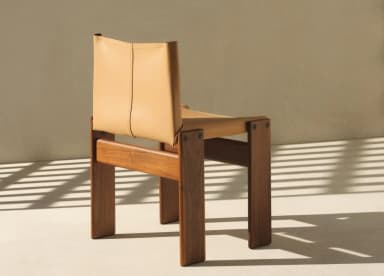 A low-profile lounge chair featuring a sturdy, rectilinear wooden frame and a minimalist sling construction for the seat and backrest, crafted from tan-colored leather. The frame appears to be made from a warm-toned hardwood, possibly teak or walnut, with visible joinery or bolted connections. The leather components are thick, showing stitched seams, providing a relaxed and modern aesthetic. The chair is designed for comfort with an emphasis on natural materials and clean lines. — 3D model