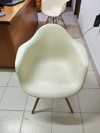 An off-white, molded plastic armchair with integrated armrests and a 'Eiffel Tower' style base consisting of splayed wooden dowel legs reinforced with black metal cross-supports. The chair is positioned on a light-colored tiled floor. — 3D model