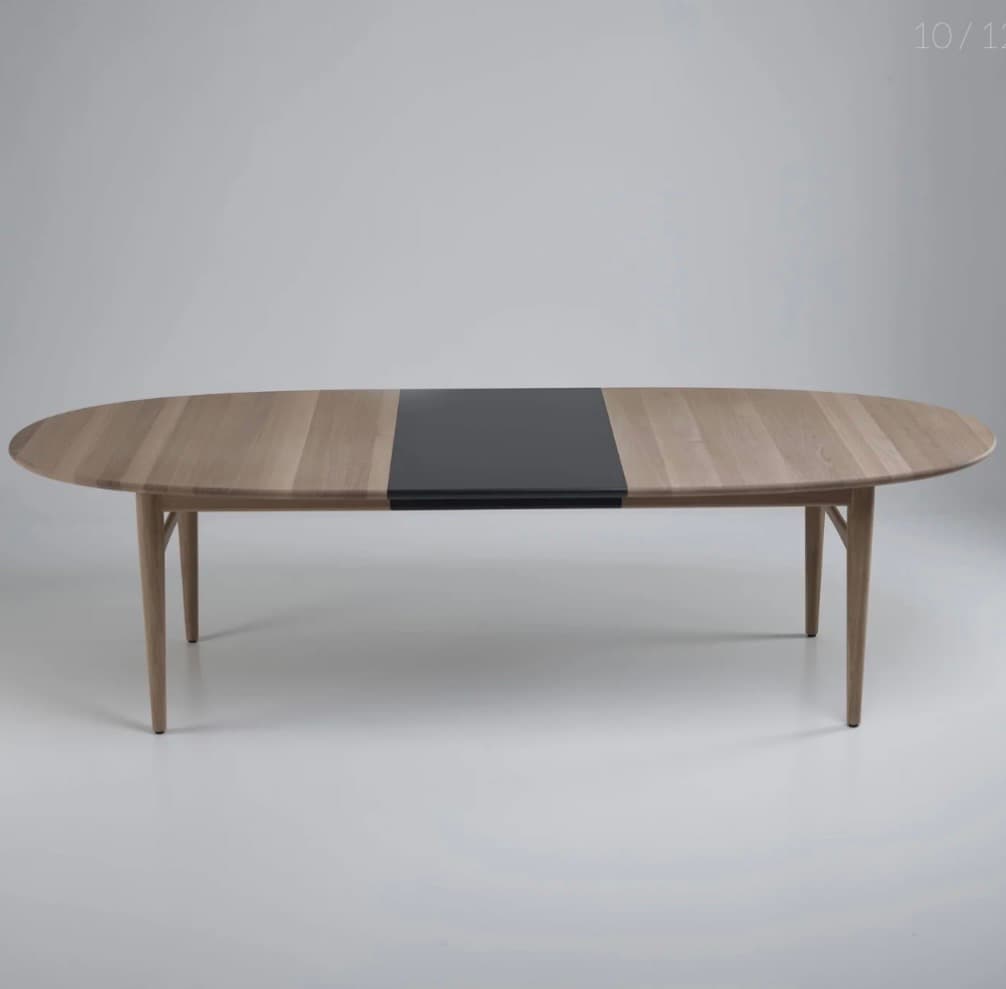 An oval dining table with a light wood finish and a contrasting dark inlay in the center. The table has four tapered legs that extend outwards from the base. — 3D model