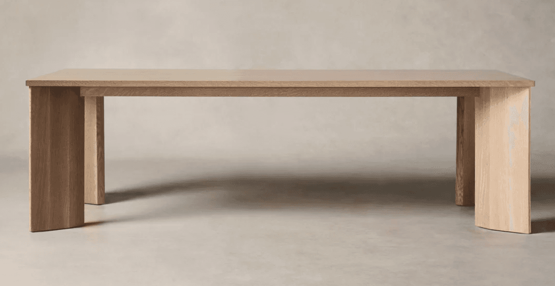 A robust, rectangular dining table crafted from light-colored wood, likely oak, featuring a thick tabletop and substantial, minimalist slab legs that curve slightly at the base, projecting a contemporary aesthetic. — 3D model