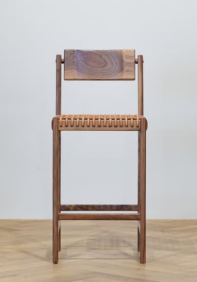 A tall bar stool with a light wood frame and a woven seat and backrest. The frame consists of four vertical legs connected by horizontal stretchers. The seat is made of intertwined leather straps, and the backrest is a solid, slightly curved wooden piece attached to the upper part of the frame. — 3D model