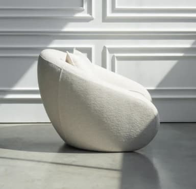 A contemporary lounge chair with a rounded, organic silhouette, fully upholstered in a textured, off-white fabric, and featuring a loose back cushion. — 3D model