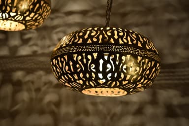 An ornate, globular pendant light crafted from dark brass or a similar metal, featuring intricate, hand-pierced cutout patterns that create a decorative glow when illuminated. The light fixture hangs from a chain, and its design is strongly reminiscent of traditional Moroccan or Middle Eastern artistry. The light source within emits a warm, inviting glow through the perforations. — 3D model