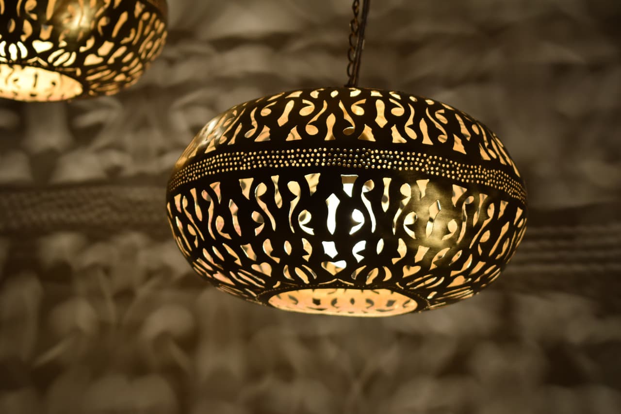 An ornate, globular pendant light crafted from dark brass or a similar metal, featuring intricate, hand-pierced cutout patterns that create a decorative glow when illuminated. The light fixture hangs from a chain, and its design is strongly reminiscent of traditional Moroccan or Middle Eastern artistry. The light source within emits a warm, inviting glow through the perforations. — 3D model