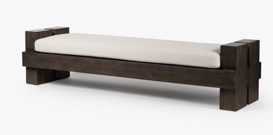 A contemporary bench with a dark wood frame and a light-colored upholstered seat. The frame features a blocky, geometric design with staggered vertical elements at each end, creating a robust and architectural appearance. The seat is a simple rectangular cushion, providing a contrast in texture and color to the solid wood base. The bench is presented against a plain white background, highlighting its form and details. — 3D model