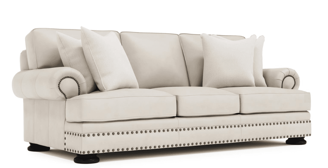 A three-seater sofa upholstered in cream-colored leather or faux leather, featuring rolled arms, decorative nailhead trim along the base and armrests, and dark bun feet. — 3D model