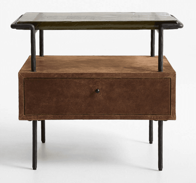 A nightstand featuring a distressed brown leather-wrapped body with a single drawer, supported by a black industrial-style metal frame and legs. The top surface is an olive green, textured material, possibly stone or a stone-look composite, which sits within the metal frame. An open shelf is present above the drawer. — 3D model