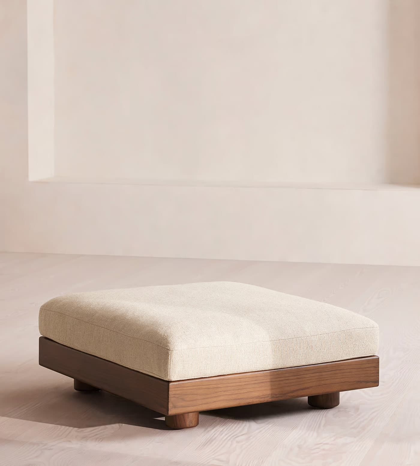 A rectangular ottoman with a cushioned top and a wooden base. The base has a low profile and is supported by four cylindrical wooden legs. The upholstery appears to be a textured fabric. — 3D model