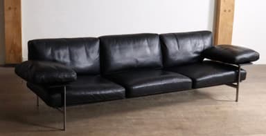 A modern three-seater sofa upholstered in black leather, featuring a minimalist design with a visible slim metal frame. It has three individual seat cushions, three back cushions, and detached, cushioned armrests, all in matching black leather. The sofa stands on slender metal legs, contributing to its sleek, elevated profile. — 3D model