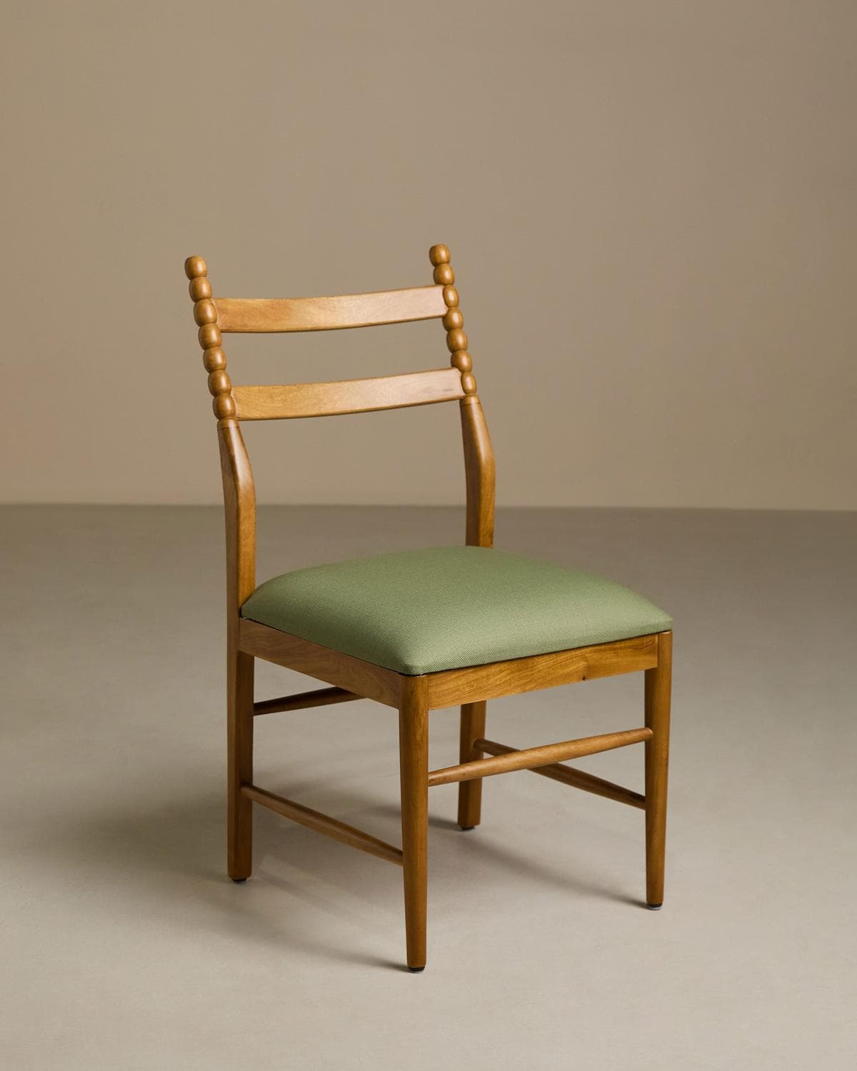 A wooden dining chair with a light natural wood finish and an upholstered green seat cushion. The chair features a backrest with two horizontal slats and vertical back posts adorned with a beaded, turned detail. The legs are straight and connected by simple stretchers, providing stability. — 3D model