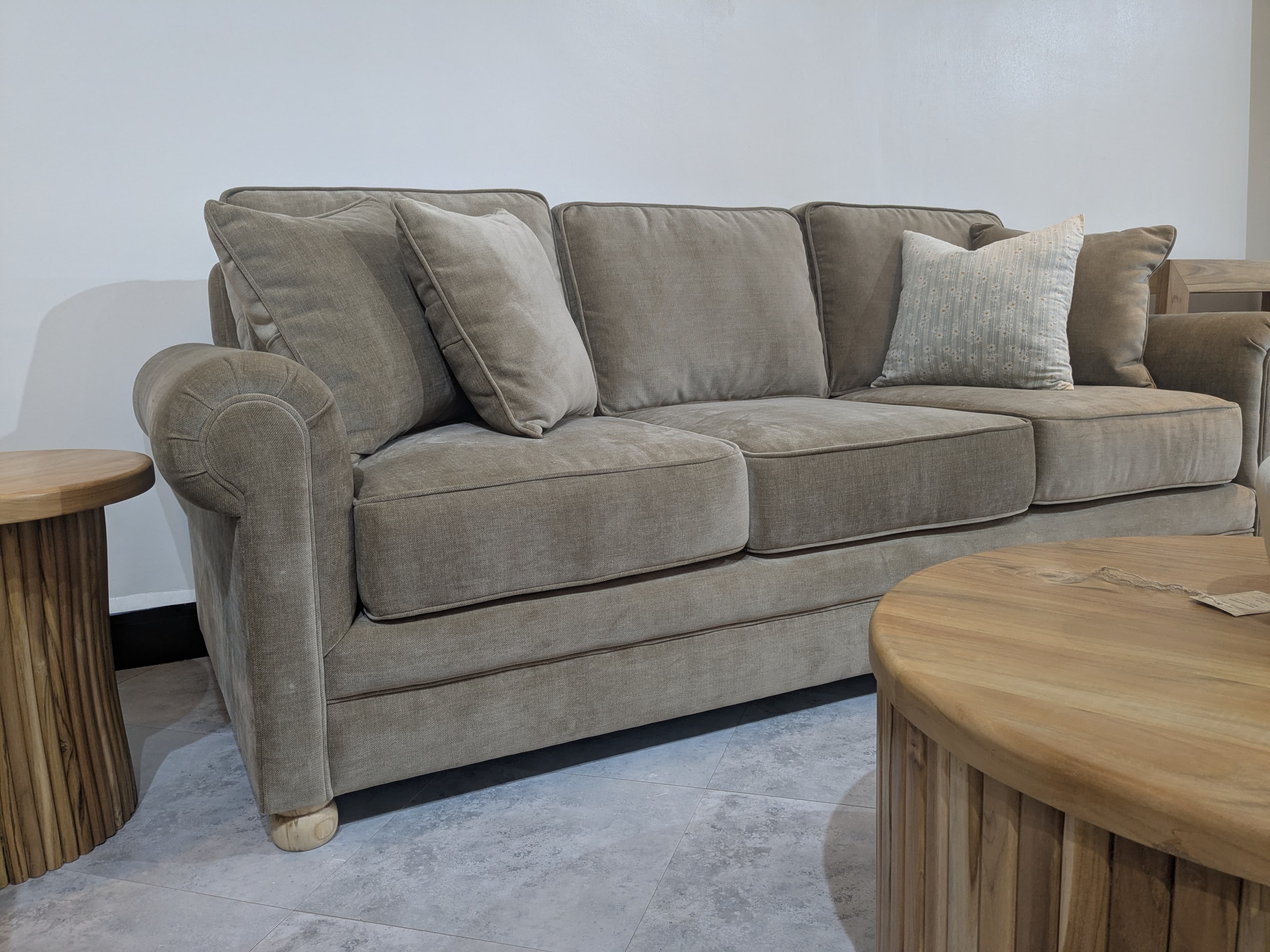 A traditional-style three-seater sofa upholstered in a neutral beige fabric, featuring classic rolled arms, loose back and seat cushions, and two decorative throw pillows. The sofa is supported by short, turned wooden feet. — 3D model
