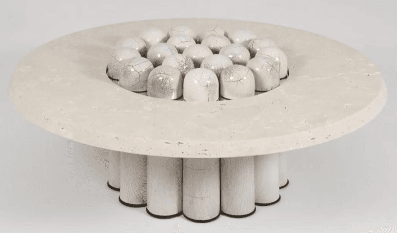 A circular coffee table with a travertine-like top featuring a central decorative element composed of numerous small, rounded ceramic pieces arranged in a circular pattern. The base of the table consists of multiple cylindrical wooden elements, painted white and arranged radially. — 3D model