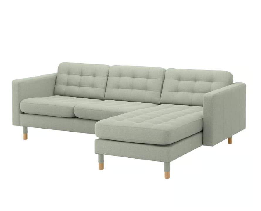 A light sage green fabric sectional sofa with a right-hand facing chaise lounge. The sofa features tufted back and seat cushions, square armrests, and is supported by four light-toned, tapered wooden legs on each section. The upholstery has a woven texture. — 3D model