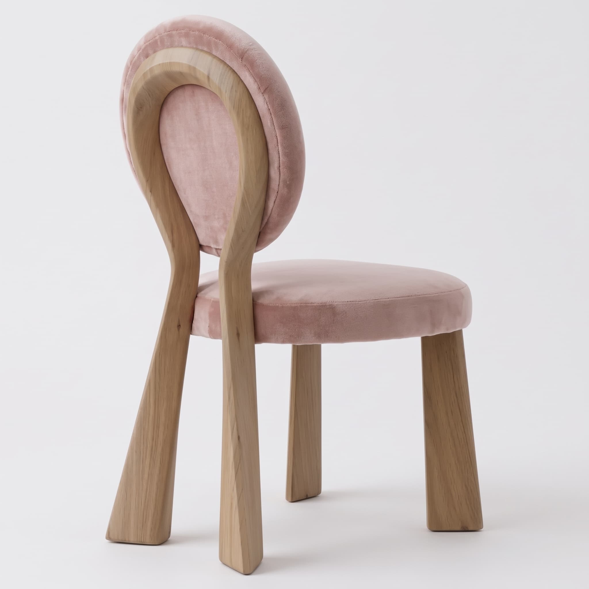 A contemporary chair featuring a unique sculptural backrest crafted from light-toned wood, complementing a plush pink velvet upholstered seat and back pad. The wooden frame extends downwards to form the four sturdy legs. — 3D model