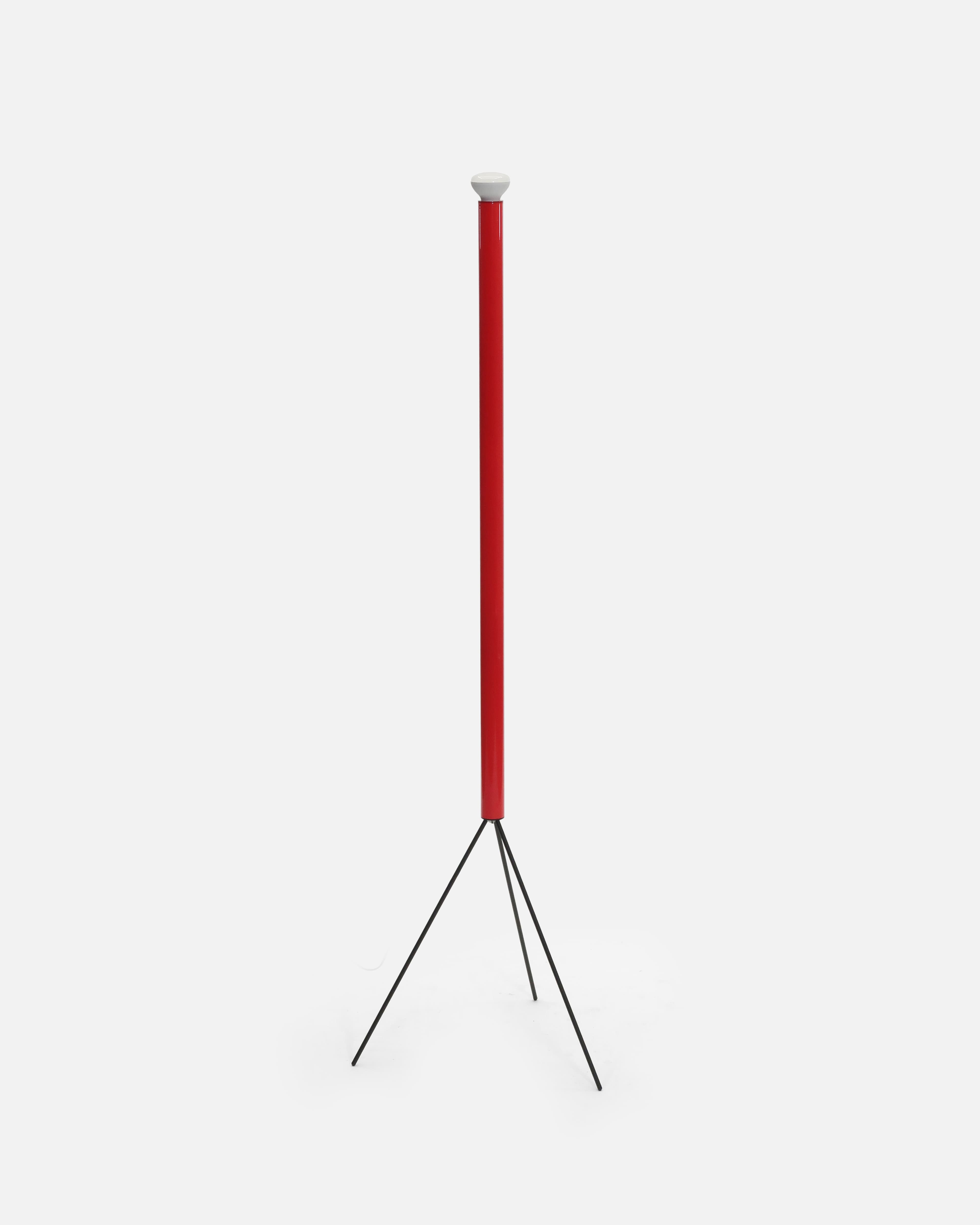 A modern floor lamp featuring a tall, slender red cylindrical column that houses the light source, supported by a minimalist black metal tripod base. A white domed diffuser caps the top of the red column. — 3D model