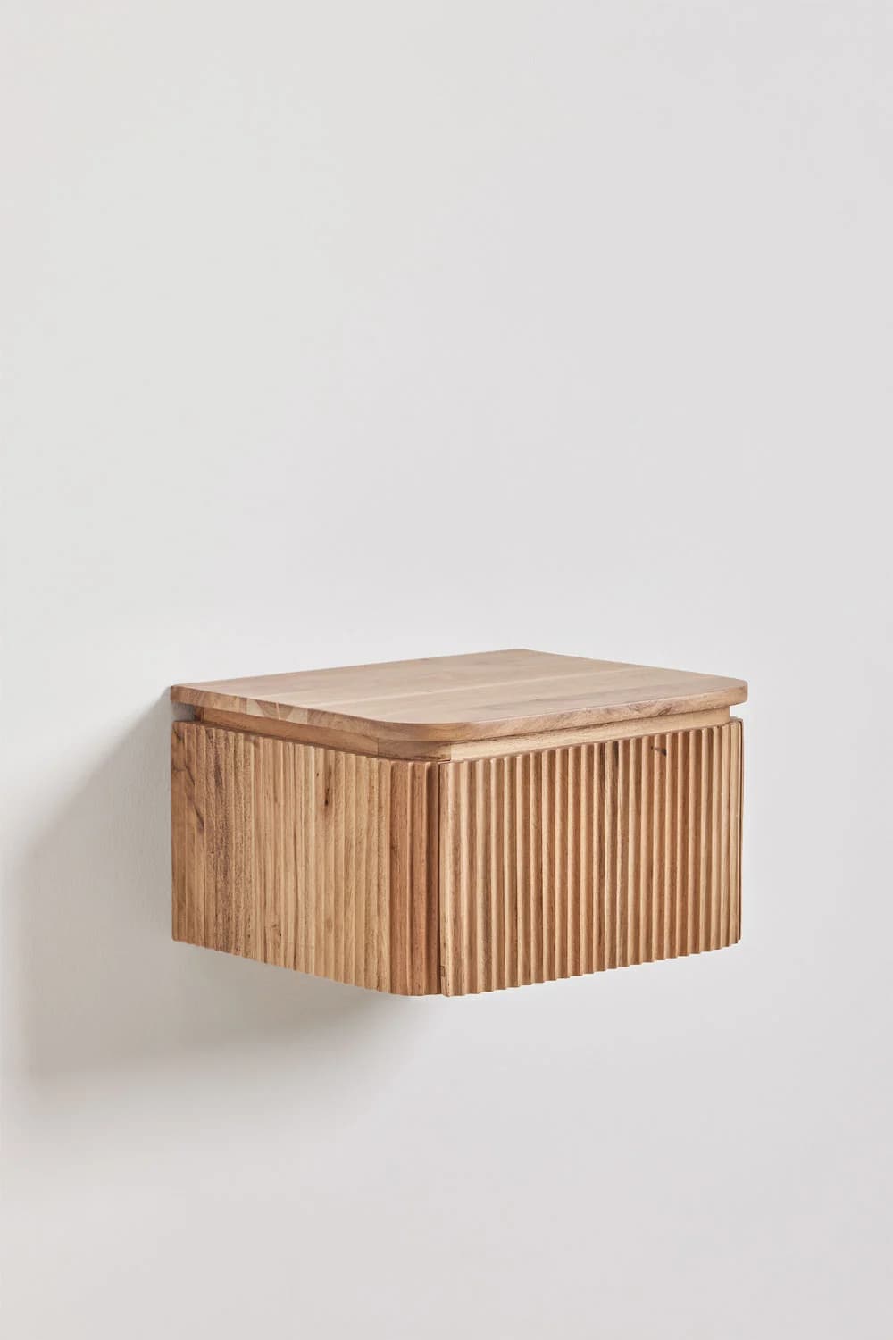A rectangular, wall-mounted wooden nightstand featuring a natural wood finish. The front and sides of the unit are adorned with a vertical reeded or fluted texture, providing a tactile and decorative element. The top surface is smooth with gently rounded edges, slightly overhanging the reeded body. A subtle seam on the front suggests a drawer or hinged door for internal storage. — 3D model