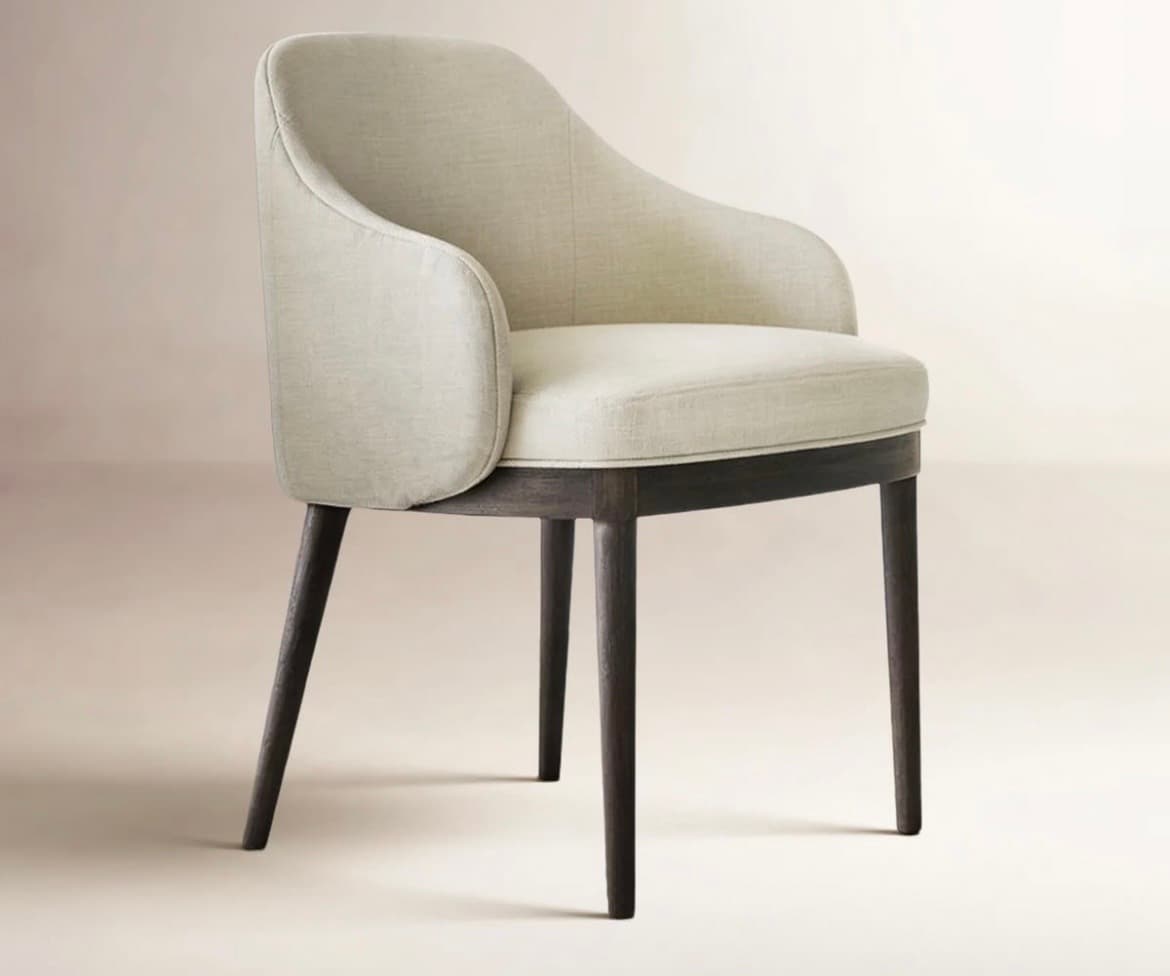 An upholstered armchair with a curved barrel back and armrests, set on four dark, tapered wooden legs. The fabric is a light, neutral color, likely a linen or bouclé blend, and the wood has an espresso finish. The design suggests a modern or contemporary aesthetic, suitable for dining or as an accent piece. — 3D model