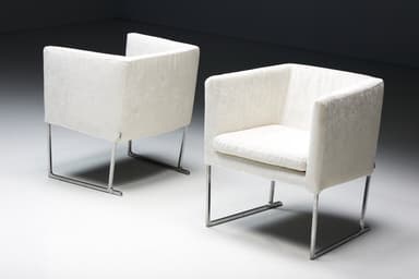 A set of four identical armchairs with a modern design. Each armchair features a cube-like upholstered seat and backrest with squared arms. The upholstery appears to be a textured fabric. The chairs are supported by a sleek, minimalist frame, likely made of polished metal, elevating them slightly off the ground. The overall aesthetic suggests a contemporary or minimalist style. — 3D model