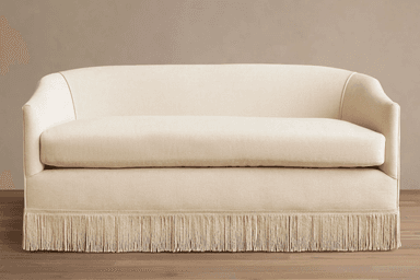 A light-colored, upholstered loveseat featuring a rounded back and integrated arms, with a distinctive fringed skirt along its base. — 3D model
