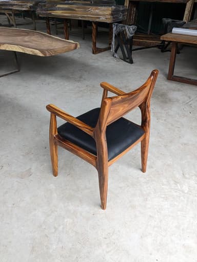 A Mid-Century Modern style dining armchair crafted from rich, dark wood with a distinct grain, featuring a contoured, integrated backrest and armrests, and an upholstered black leather seat. The chair's design emphasizes organic curves and sculpted lines. — 3D model